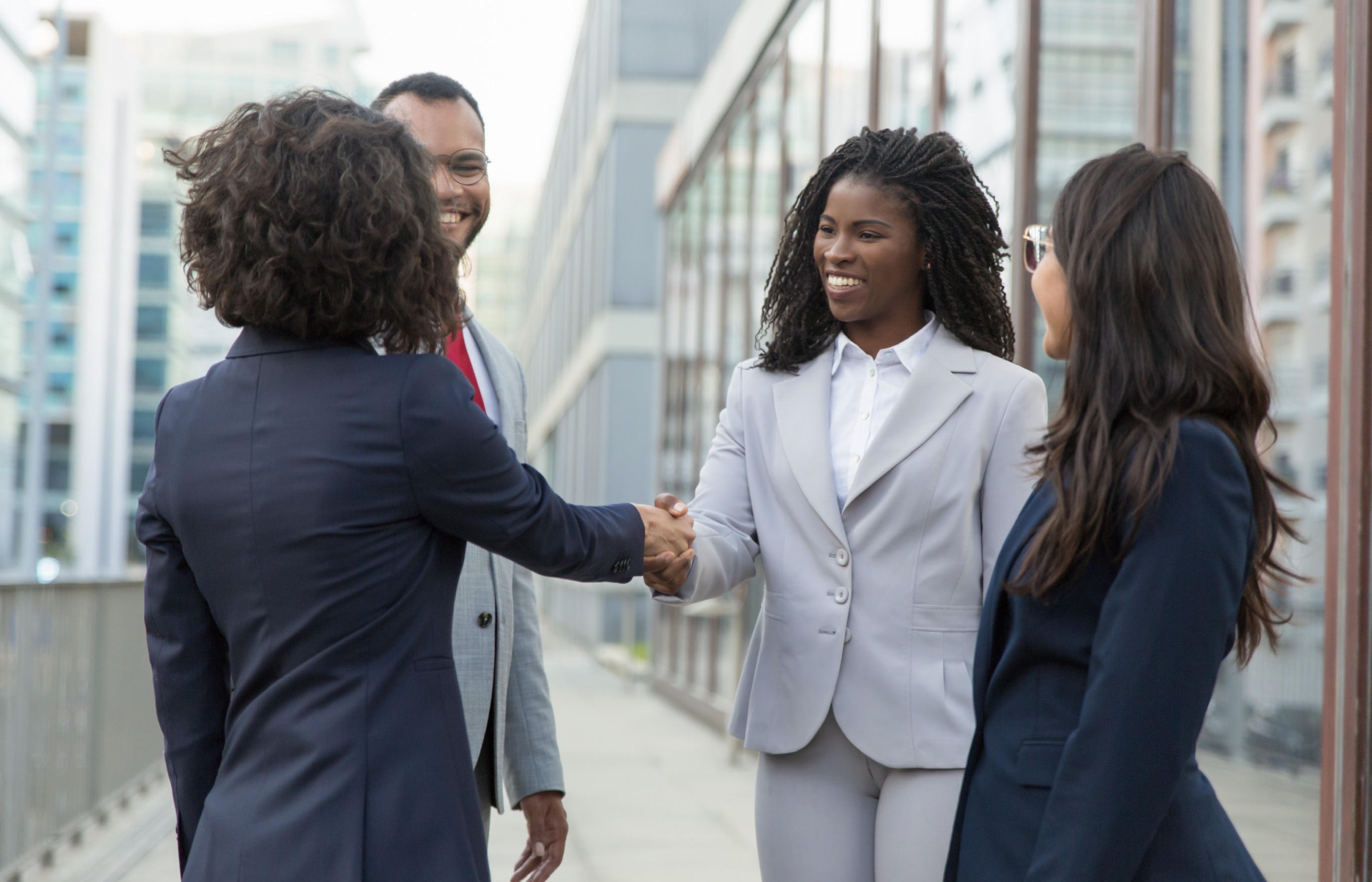 Black businesswoman greeting another executive as colleagues look on